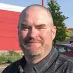 Smiling man outdoors near a red building.