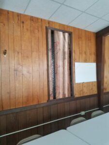 Wood-paneled room wall with insulation exposed.