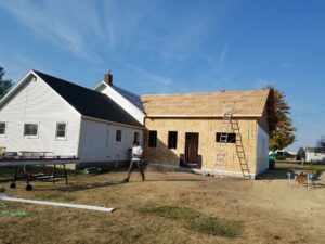 House under construction with ladder and worker nearby.