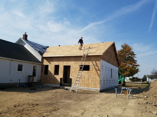 Construction worker on ladder building house roof.