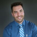 Smiling man in blue shirt and striped tie.