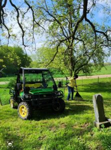 Person raking near utility vehicle in grassy area.